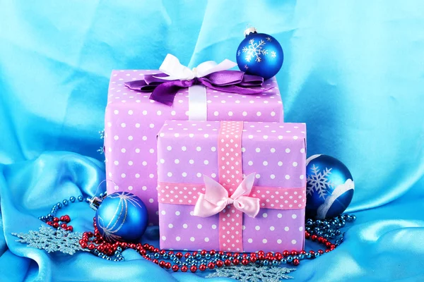 Beautiful purple in peas gifts with blue Christmas balls, snowflakes and beads on blue background — Stock Photo, Image