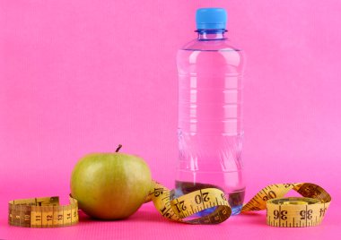 şişe su, elma ve pembe bir arka plan üzerinde ölçüm bandı