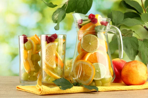 Kruik en glazen met citrusvruchten en frambozen, op groene achtergrond — Stockfoto