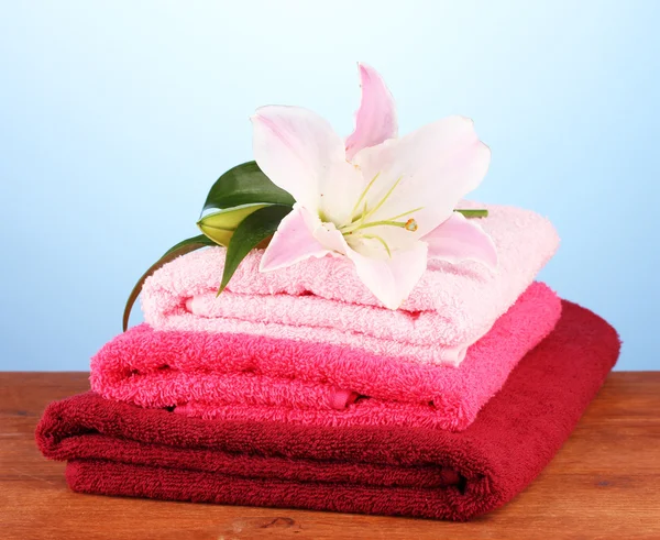 Stack of towels with pink lily on blue background — Stock Photo, Image