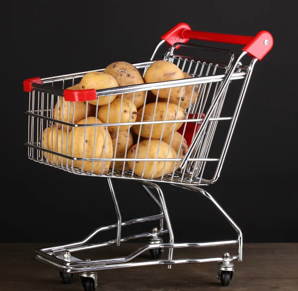 Reife Kartoffeln im Einkaufswagen auf Holztisch vor schwarzem Hintergrund — Stockfoto