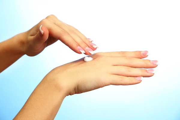 Belles mains de femme avec de la crème, sur fond bleu — Photo