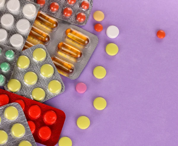 Capsules and pills packed in blisters on purple background — Stock Photo, Image