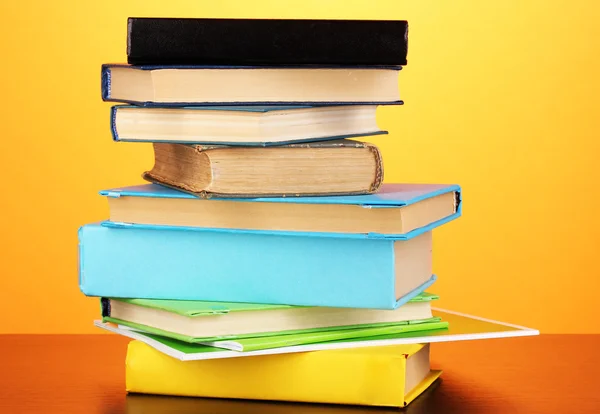 Stapel interessante boeken en de tijdschriften op houten tafel op oranje achtergrond — Stockfoto