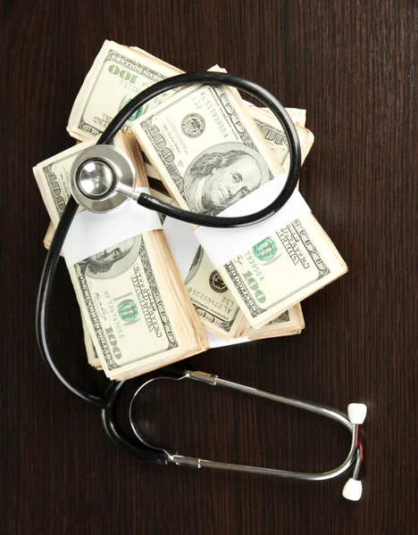 Healthcare cost concept: stethoscope and dollars on wooden background — Stock Photo, Image