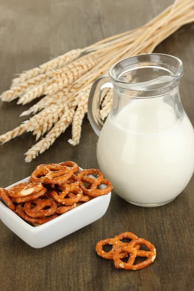 Tasty pretzels in white bowl and milk jug on wooden table close-up — Stock Photo, Image