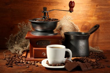 Coffee grinder, turk and cup of coffee on brown wooden background clipart