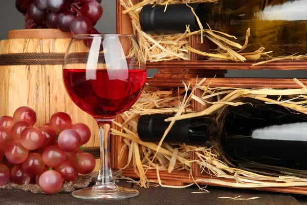 Caja de madera con botellas de vino, barril, vino y uva sobre mesa de madera sobre fondo gris — Foto de Stock