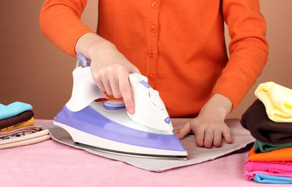 Mujer joven planchando su ropa, sobre fondo marrón — Foto de Stock