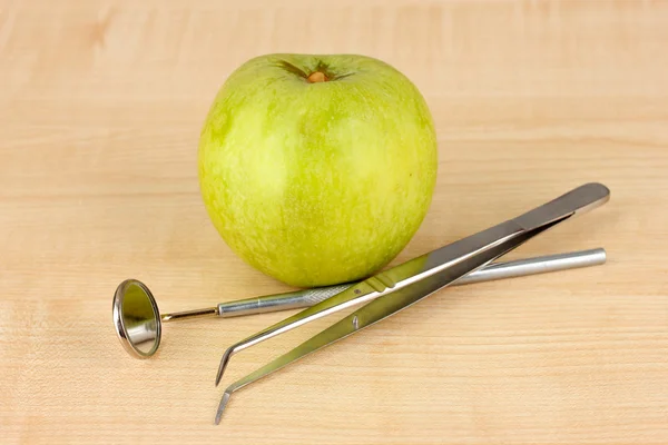 Grüner Apfel und zahnärztliche Instrumente auf hölzernem Hintergrund — Stockfoto