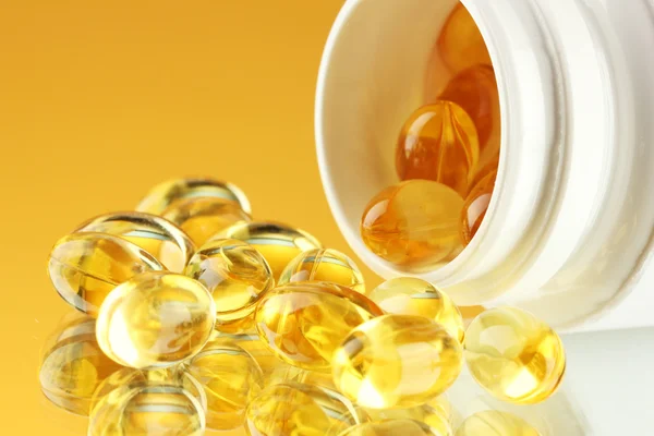 Capsules in bottle, on yellow background — Stock Photo, Image