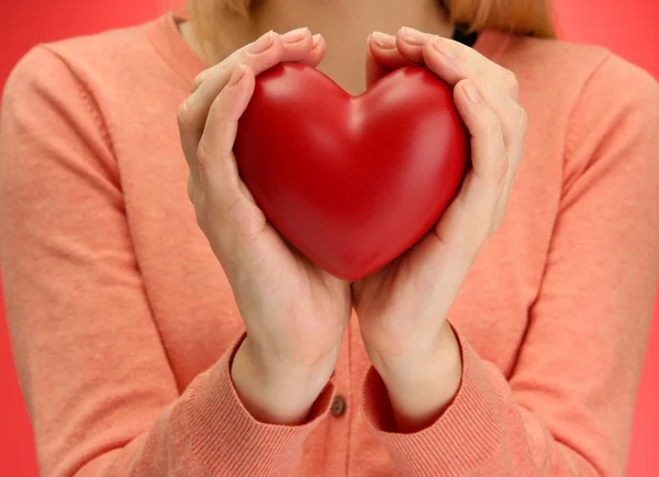 Coeur rouge dans les mains de la femme, sur fond rouge — Photo