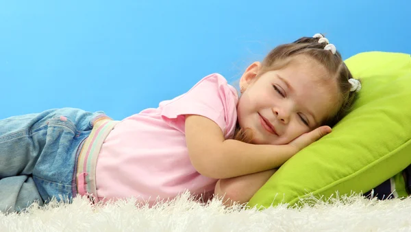 Söta lilla flicka sover på färgglada kuddar, på blå bakgrund — Stockfoto