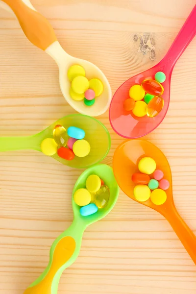 Cucharas de plástico con píldoras de color sobre fondo de madera —  Fotos de Stock