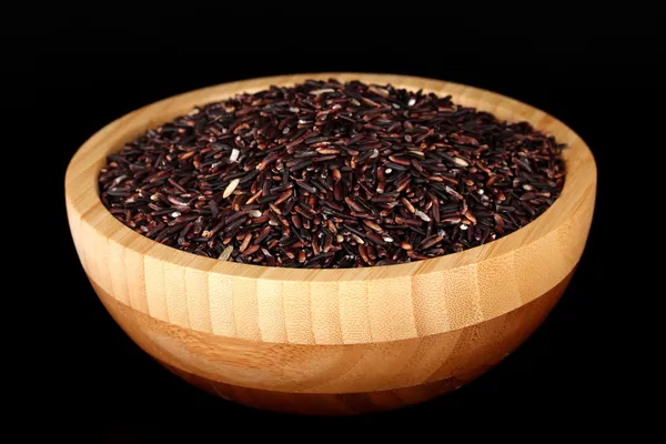 Black rice in wooden bowl isolated on black — Stock Photo, Image