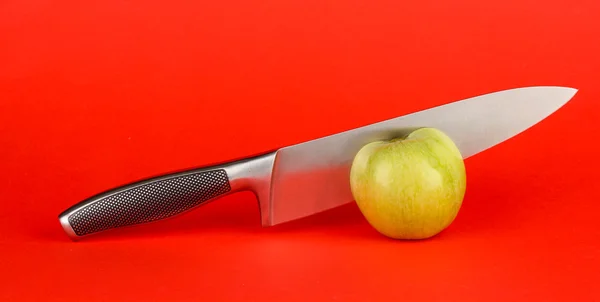 Green apple and knife on red background — Stock Photo, Image