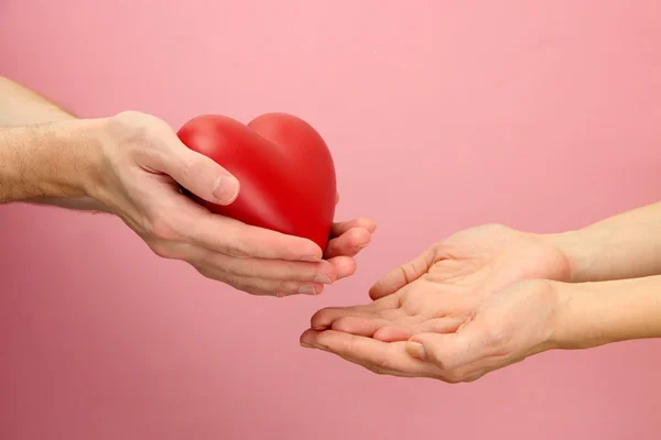 Red heart in woman and man hands, on pink background — Stock Photo, Image
