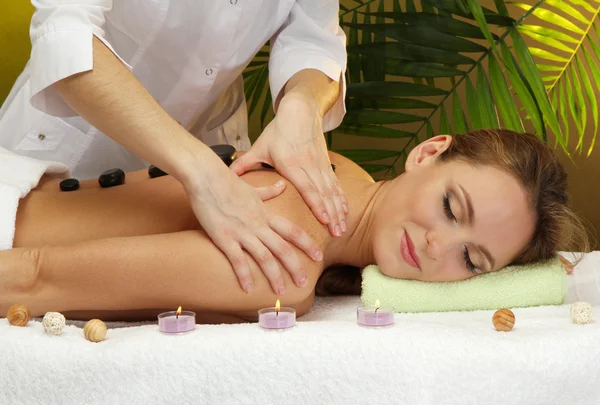 Beautiful young woman in spa salon getting massage with spa stones, on green background — Stock Photo, Image