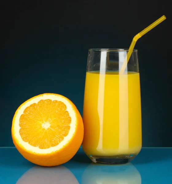 Heerlijke sinaasappelsap in glas en oranje ernaast op donker blauwe achtergrond — Stockfoto