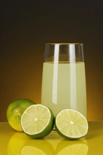 Köstlicher Zitronensaft im Glas und Limetten daneben auf dunkelorangefarbenem Hintergrund — Stockfoto