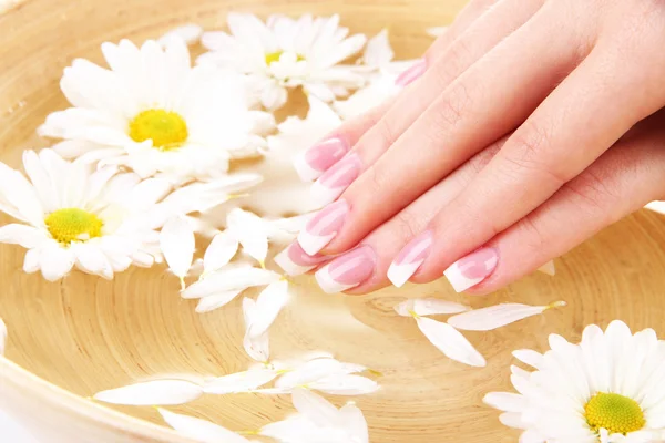 Mãos de mulher com manicure francês e flores em tigela de bambu com água — Fotografia de Stock