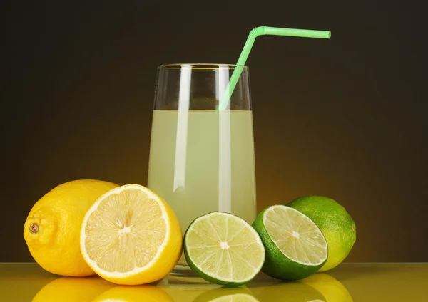 Delicioso zumo de limón en vidrio y limas y limones junto a él sobre fondo naranja oscuro — Foto de Stock