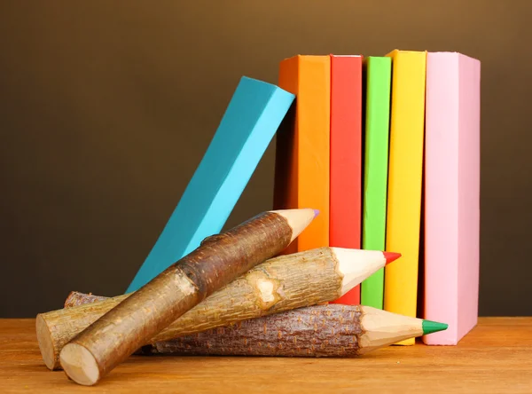 Lápis de madeira coloridos com livros sobre mesa de madeira sobre fundo marrom — Fotografia de Stock