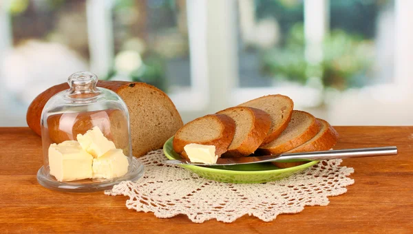 Butter on glass saucer with glass cover surrounded by bread, on bright background — Stock Photo, Image