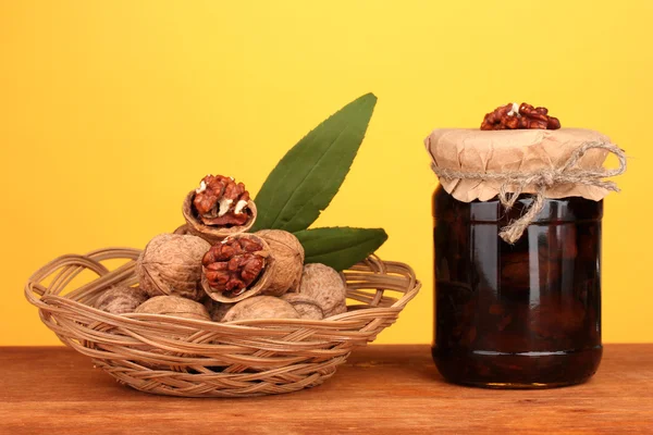 Marmellata-vaso di noci su tavolo di legno e un cesto con noci su sfondo arancione — Foto Stock