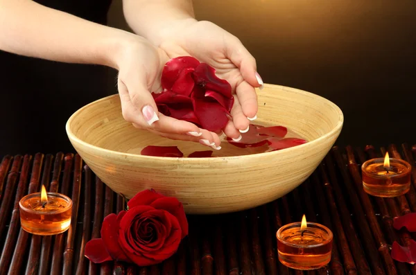 Woman hands with wooden bowl of water with petals, on brown background — Stock Photo, Image