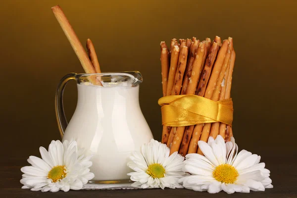 Palitos crocantes saborosos com jarro com creme de leite na mesa de madeira no fundo amarelo — Fotografia de Stock