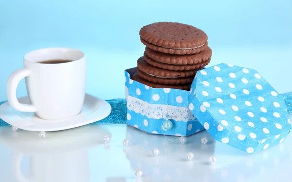Biscoitos de chocolate com camada cremosa e xícara de café no fundo azul — Fotografia de Stock