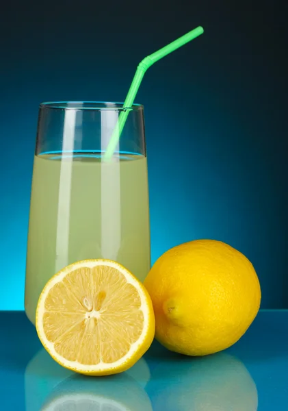 Délicieux jus de citron en verre et citrons à côté sur fond bleu foncé — Photo