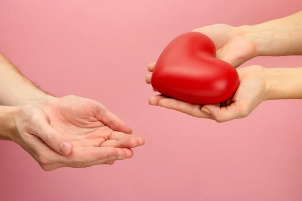 Red heart in woman and man hands, on pink background — Stock Photo, Image