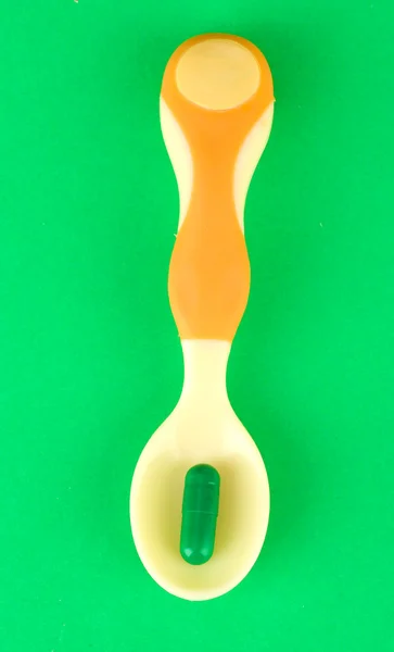 Yeşil arka plan üzerinde renkli hapları ile plastik kaşık — Stok fotoğraf