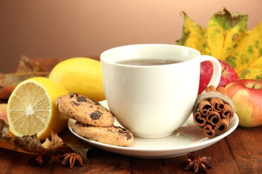 Kahverengi arka planda bir fincan sıcak çay ve sonbahar yaprakları.