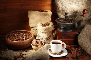 Coffee grinder and cup of coffee on brown wooden background clipart