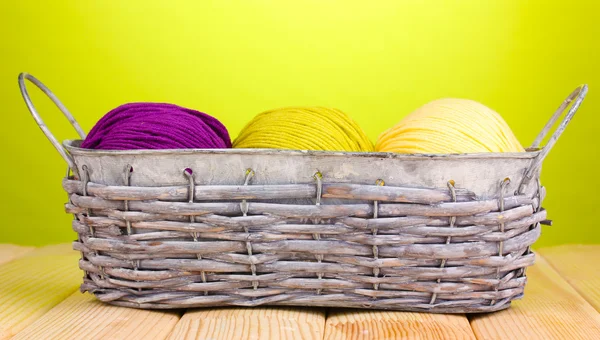 Hilos brillantes en cesta sobre mesa de madera sobre fondo verde —  Fotos de Stock