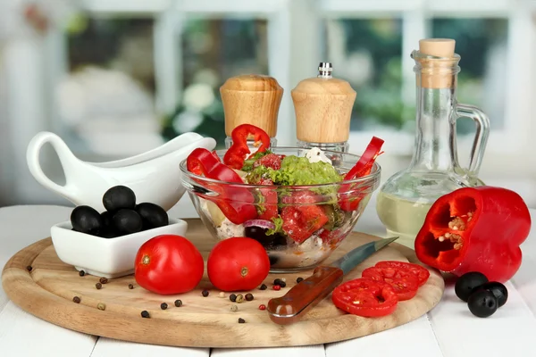 Salada grega fresca em taça de vidro cercada por ingredientes para cozinhar em mesa de madeira no fundo da janela — Fotografia de Stock