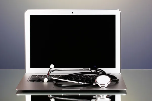 Zilveren laptop met een stethoscoop op grijze achtergrond met reflectie — Stockfoto