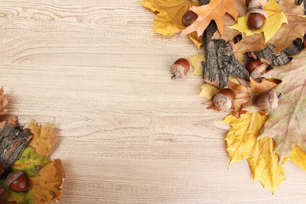 Bellotas marrones sobre hojas de otoño, sobre fondo de madera — Foto de Stock