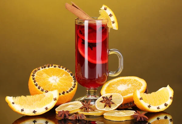 Fragrant mulled wine in glass with spices and oranges around on yellow background — Stock Photo, Image