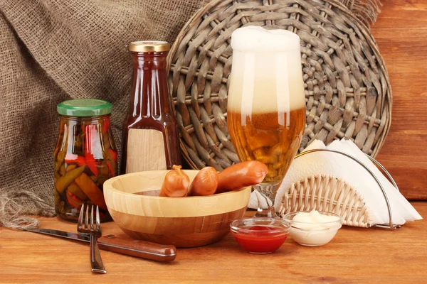 Cerveza y embutidos a la parrilla sobre mesa de madera sobre fondo de saco — Foto de Stock