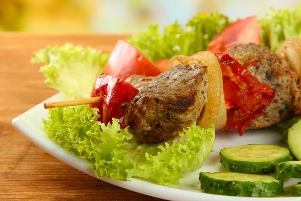 Välsmakande grillat kött och grönsaker på spett på tallrik, på träbord — Stockfoto