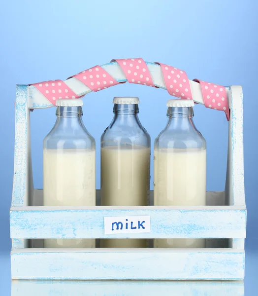 Milk in bottles in wooden box on blue background — Stock Photo, Image