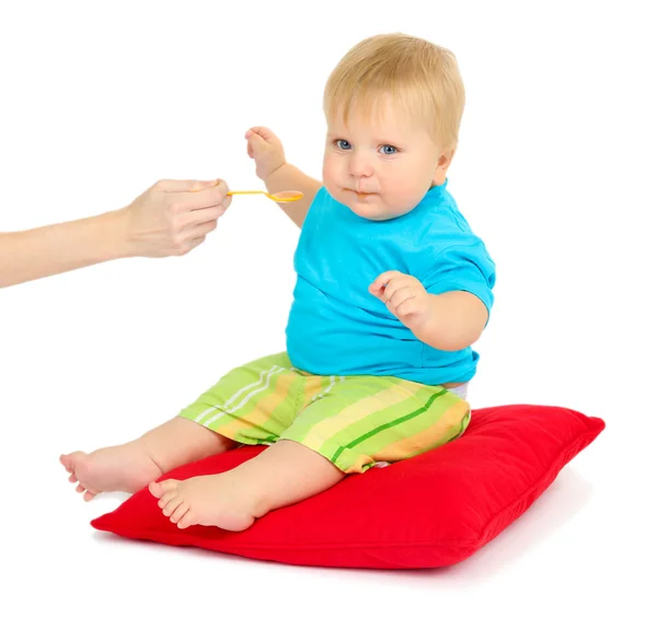 Niño sentado en la almohada roja y comiendo puré de manzana, aislado en blanco —  Fotos de Stock