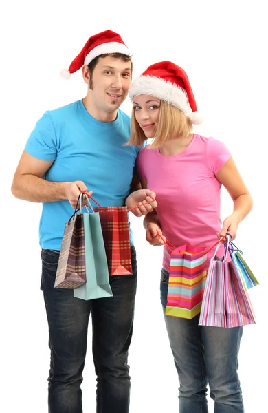 Jovem casal em Santa chapéus de compras e segurando muitos sacos de compras isolados no branco — Fotografia de Stock