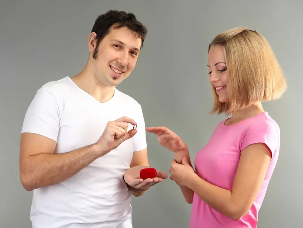 Молодой человек делает предложение о браке и дарит кольцо женщине на сером фоне — стоковое фото