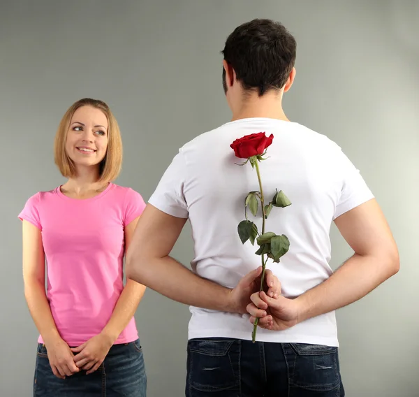 Liefdevolle man met rode roos voor zijn vrouw op grijze achtergrond — Stockfoto