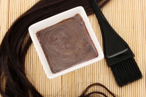 Tintura per capelli in ciotola e pennello per la colorazione dei capelli su tappetino di bambù beige, primo piano — Foto Stock